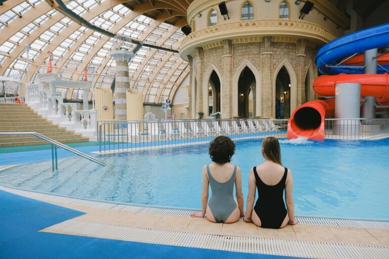 Vrouwen aan de rand van een indoor waterpark met glazen koepel en waterglijbaan
