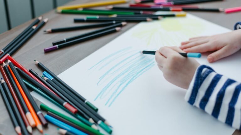Kinderhand tekent met kleurpotlood terwijl kleurpotloden op tafel liggen