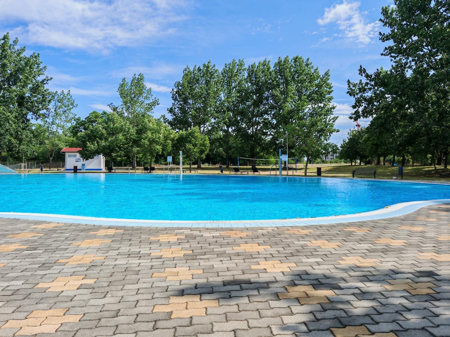 Openluchtzwembad in een park met groene bomen onder blauwe lucht — sfeerbeeld bij artikel buiten zwemmen in Antwerpen