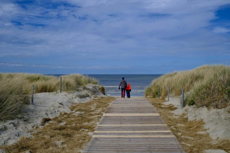 Ouder en kind lopen over een houten vlonderpad door de duinen richting het strand