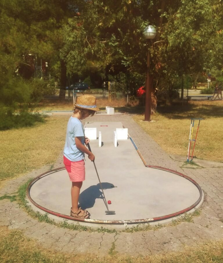Kind speelt minigolf op een vakantiepark met groene kunstgrasbaan