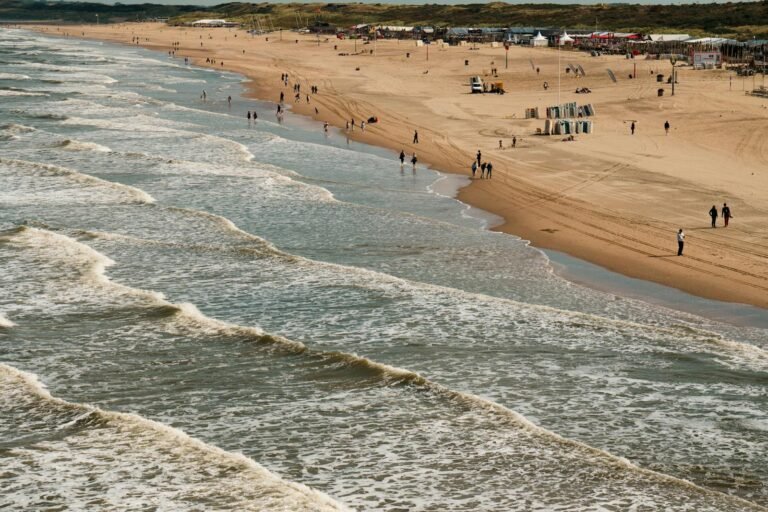 Zonnige dag aan de Nederlandse Noordzeekust met golven en strandwandelaars