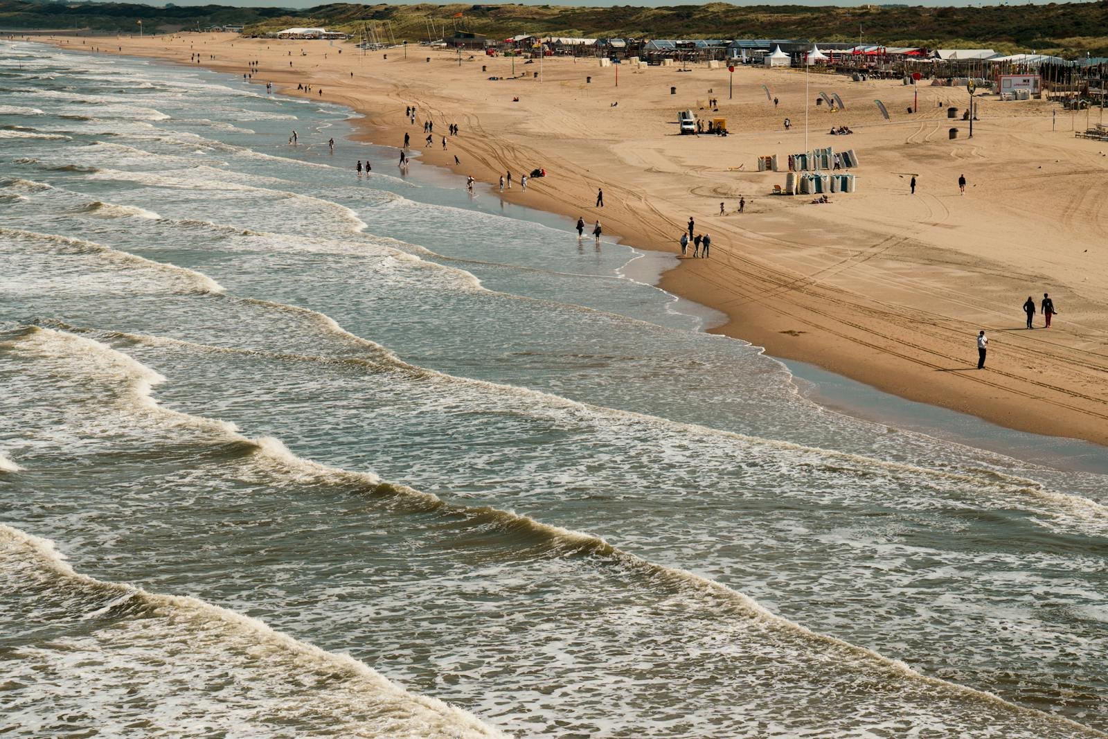 Zonnige dag aan de Nederlandse Noordzeekust met golven en strandwandelaars