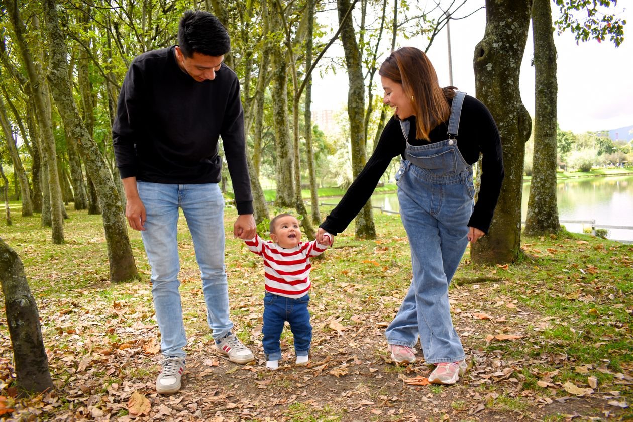 Ouders wandelen met hun baby door een herfstig park met vallende bladeren