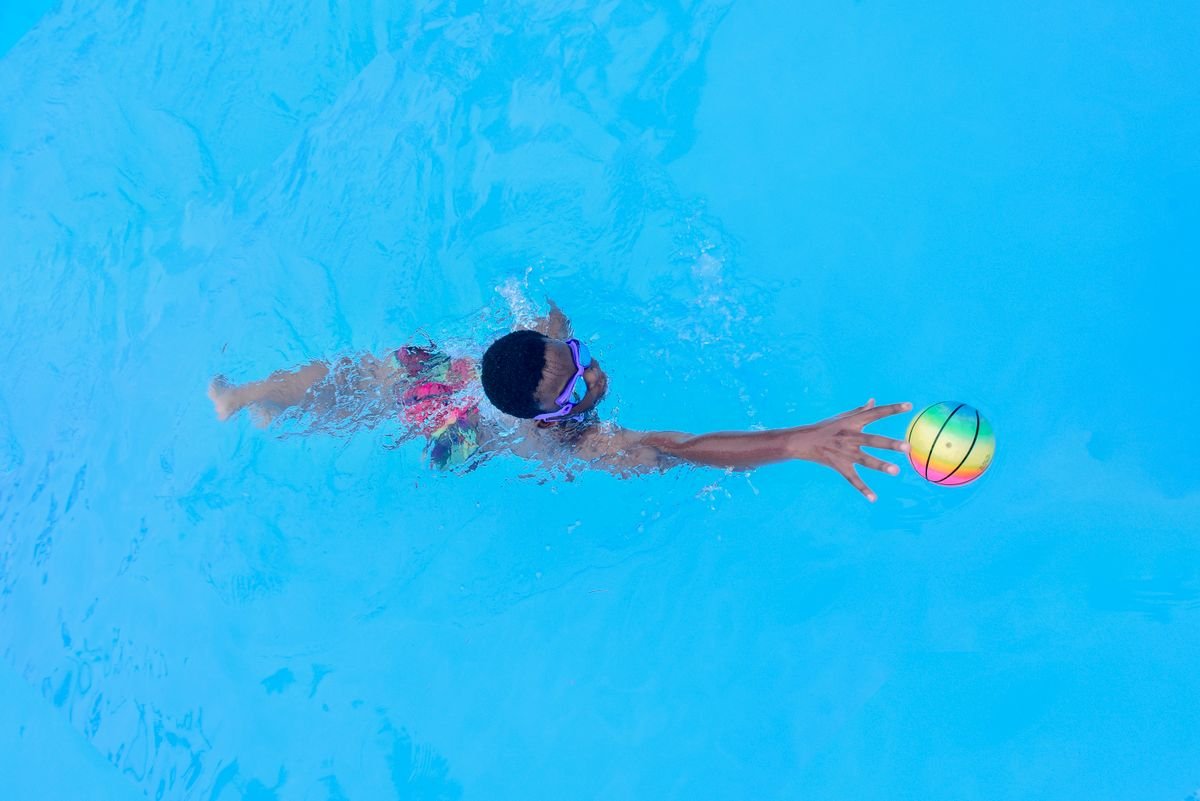 Kind zwemt onder water naar een kleurrijke bal in een helder blauw zwembad