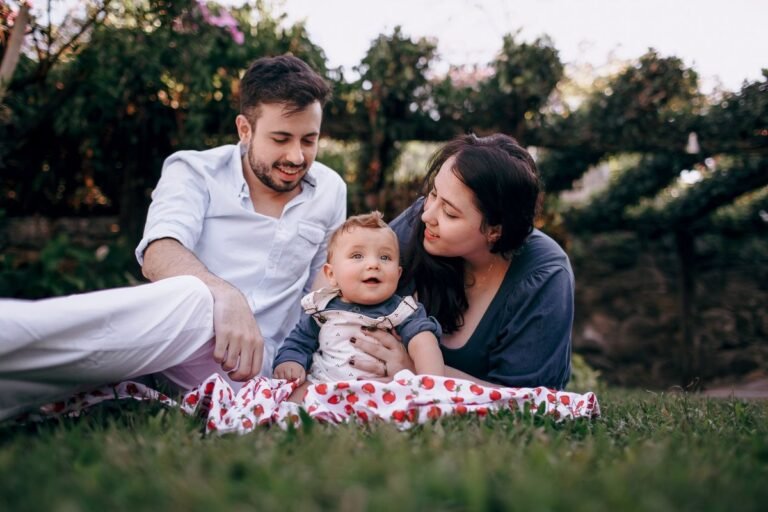 Gezin met baby op picknickkleed op groen grasveld tussen de bomen