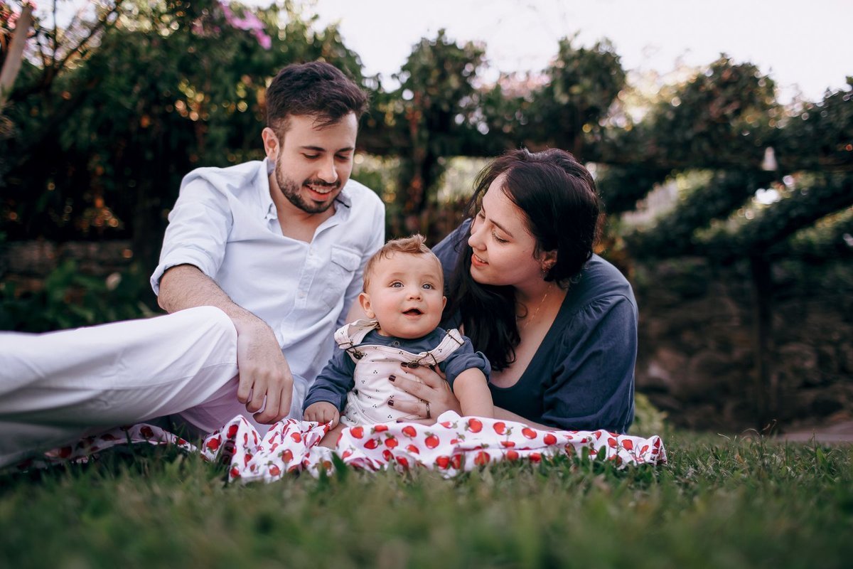 Gezin met baby op picknickkleed op groen grasveld tussen de bomen