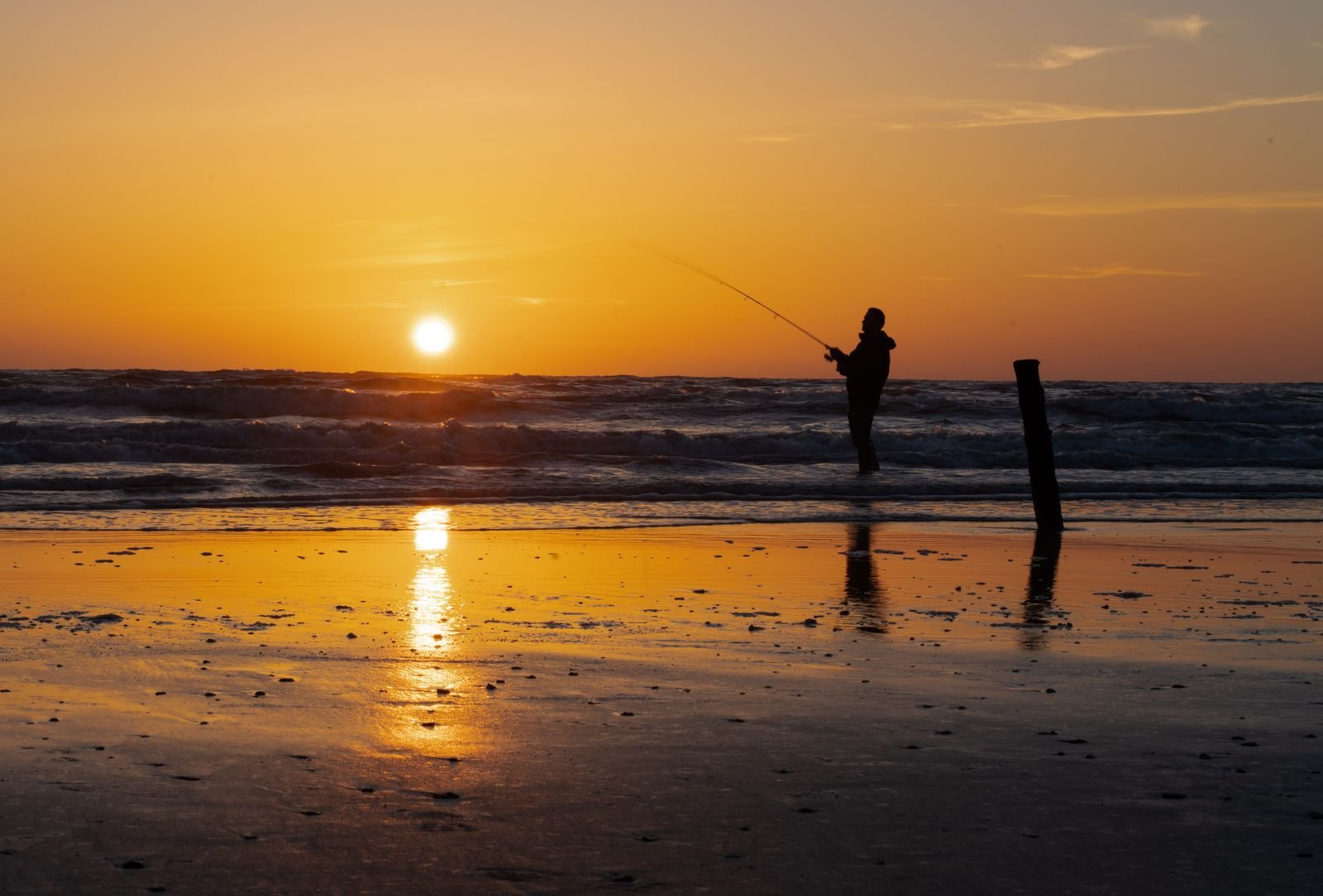 Zeevisser werpt zijn hengel uit in de branding van de Noordzee bij Nieuwvliet-Bad