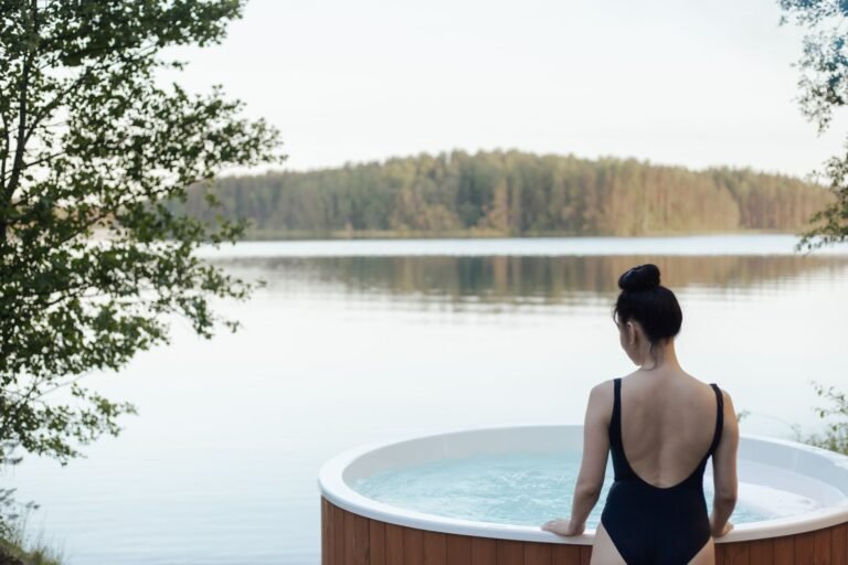 Vrouw stapt in een hottub aan een meer met bos, vakantiehuisje met hottub